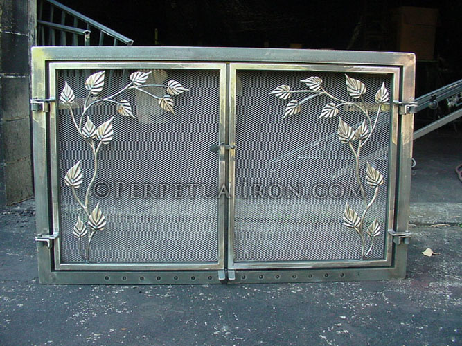 Brushed steel wrought iron fireplace screen or with leafy vine motif. The two doors dividing the fire screen mesh are mounted in a matching steel frame.